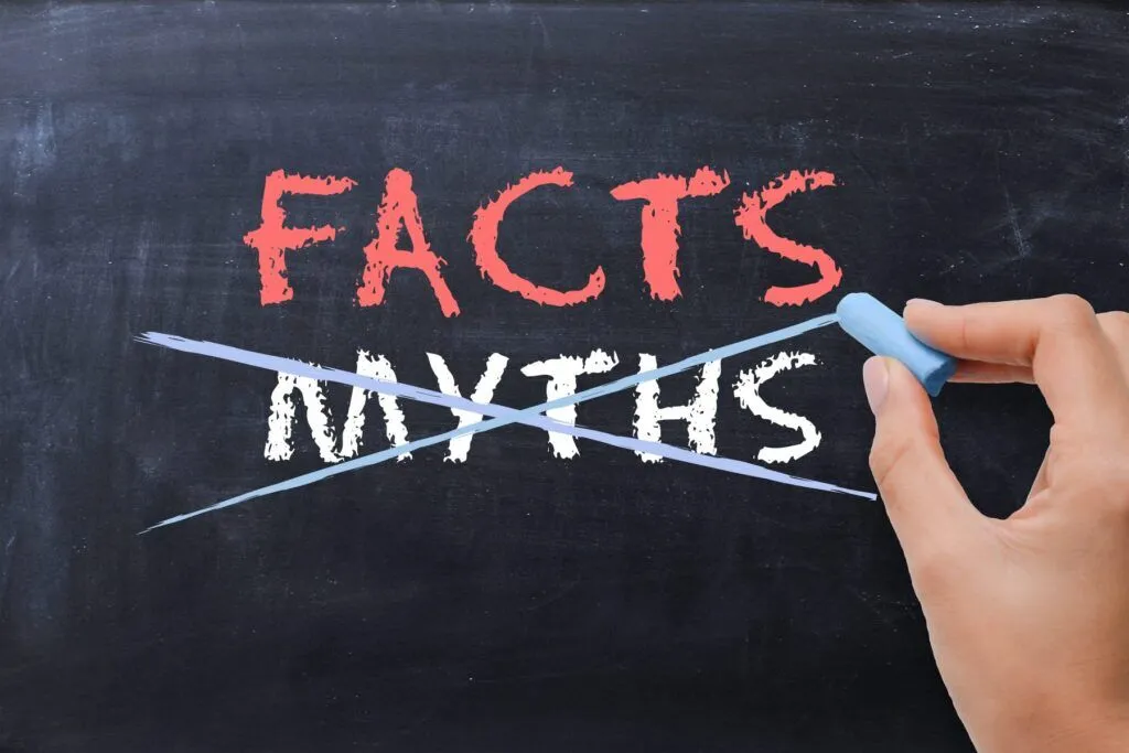 A hand writing FACTS and MYTHS on a black board with the MYTHS crossed leaving the FACTS.